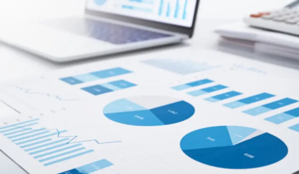 Informes con gráficos estadísticos y datos empresariales junto a un computador portátil